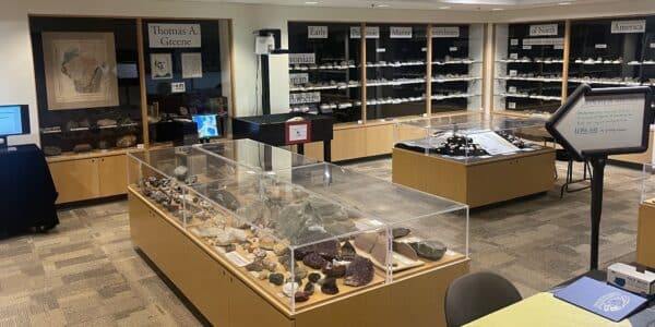 A geology museum exhibit displays various rocks and minerals in glass cases, with labeled shelves and informational signs on the walls.