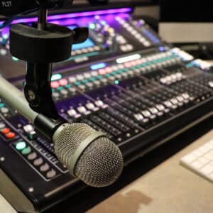 A microphone in front of a mixing console and computer keyboard in a recording studio.