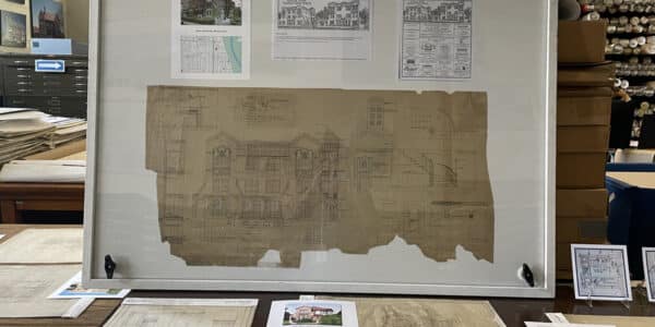 Framed architectural blueprint with reference images and drawings displayed on a table surrounded by additional architectural plans and documents.