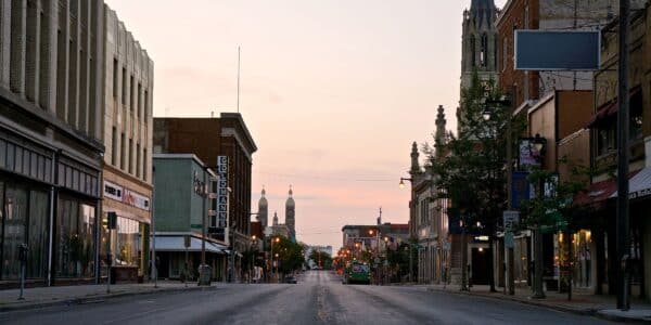 Empty city street lined with buildings, shops, and churches at dawn or dusk under a clear sky.