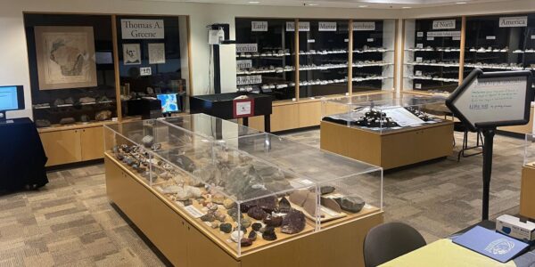 A mineral and rock exhibit room with display cases, labeled shelves, informational signs, and a computer kiosk on the left. Various specimens are showcased under glass.
