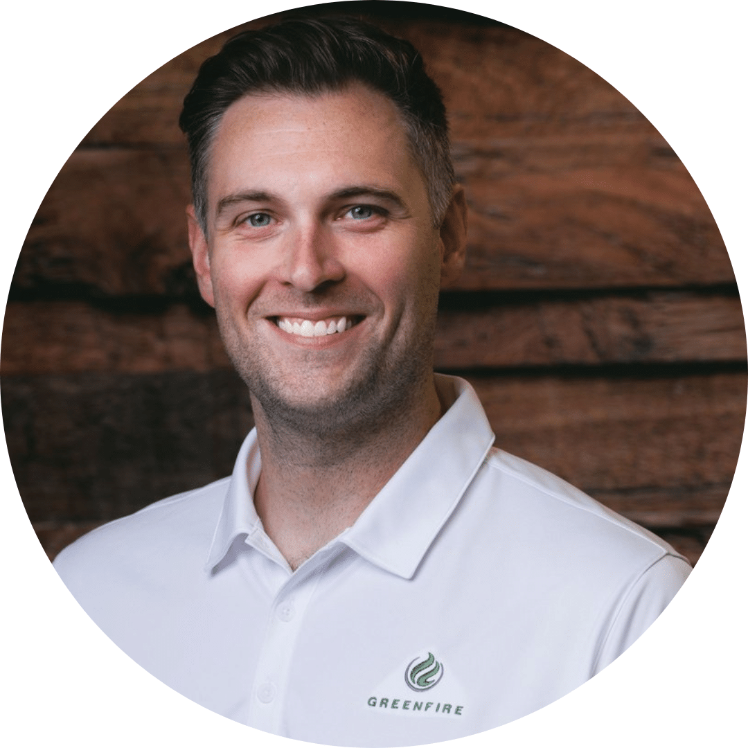 A man with short brown hair wearing a white collared shirt with the Greenfire logo, smiling in front of a wooden background.