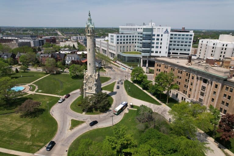Aerial view of a historic stone water tower surrounded by a circular road, with nearby modern hospital buildings and green park areas.