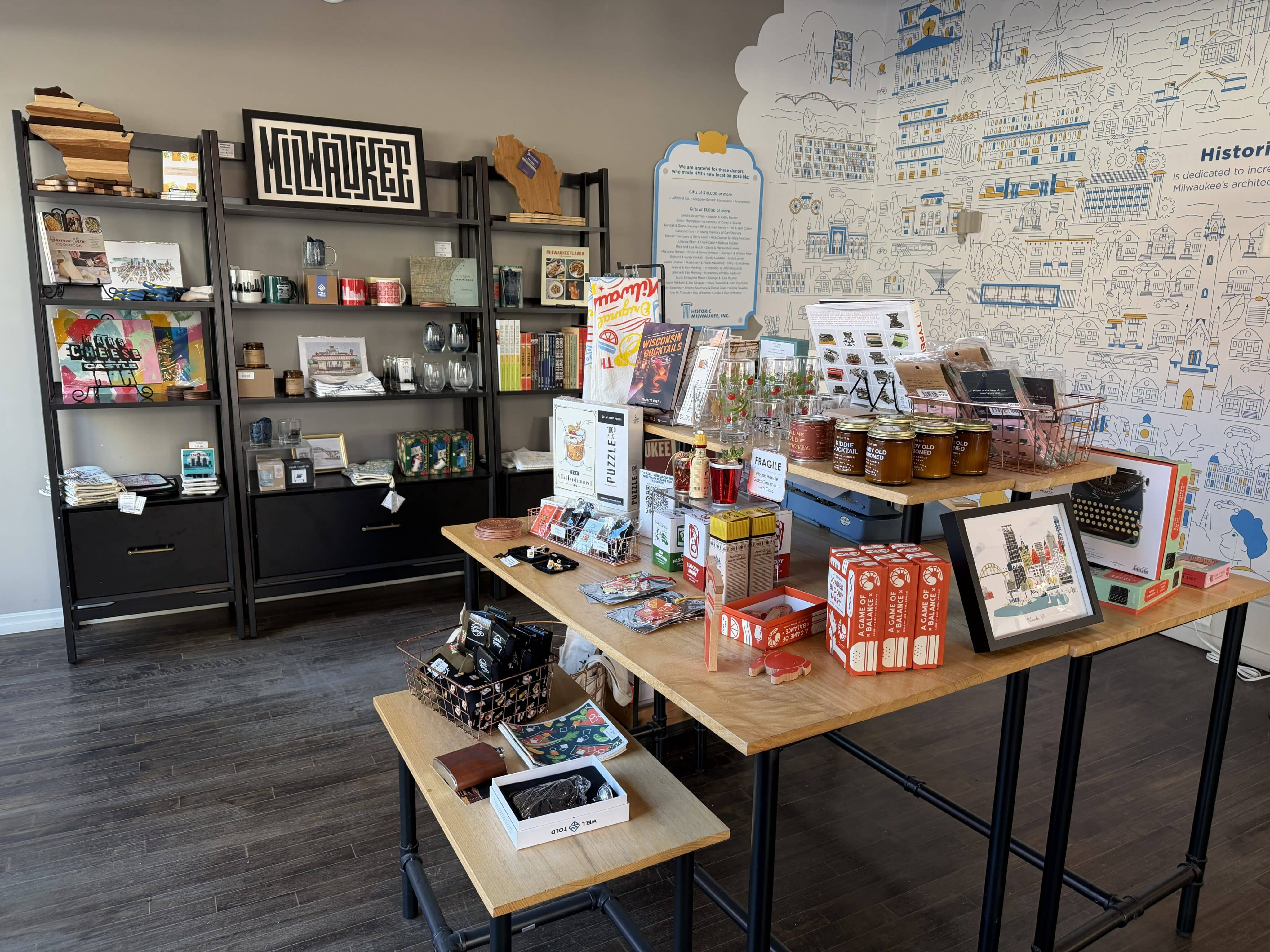 A small shop with shelves and tables displaying local goods, including mugs, jars, books, and gifts; a wall mural is visible in the background.