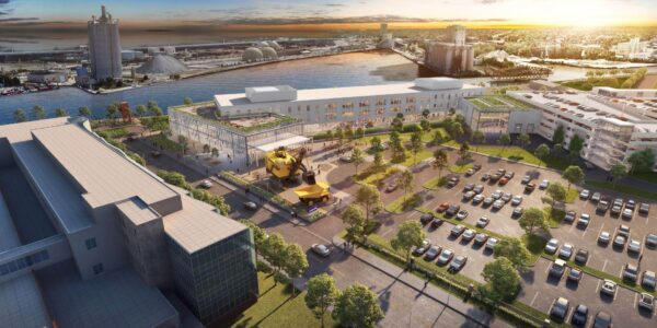 Aerial view of an industrial waterfront district with a large modern building, parking lot, and river in the background at sunset.