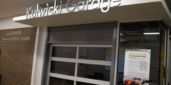 Exterior view of the Kulwicki Garage, featuring a glass garage door and a poster about a NASCAR drawing event on the right side of the entrance.
