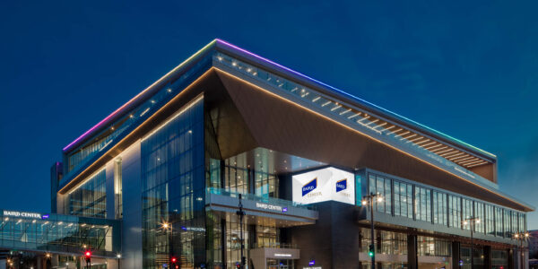 Modern glass building at night with illuminated signs reading “Baird Center”; streetlights and traffic signals are visible around the structure.