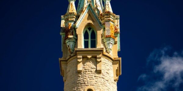 Stone tower with ornate, weathered copper details and arched windows against a deep blue sky.