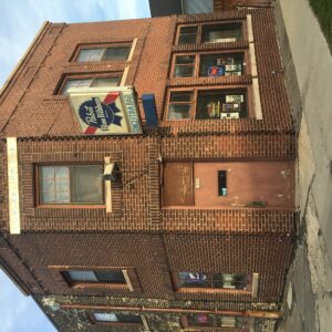 A two-story brick building with a central door, several windows, and a Pabst Blue Ribbon beer sign above the entry, seen from street level.