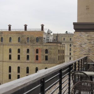 Rooftop patio with empty chairs and tables overlooks historic brick buildings on an overcast day.
