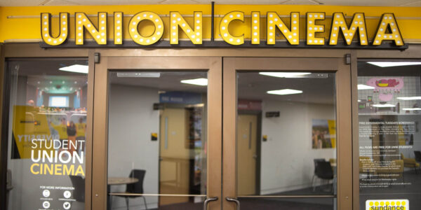 Entrance to a student union cinema with bright “Union Cinema” marquee above glass doors and posters on the sides advertising student events and film screenings.