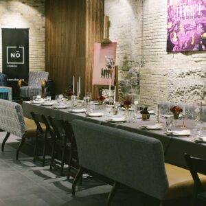 A long dining table is set with plates, glasses, and candles in a modern, industrial-style room with exposed brick walls and art on display.