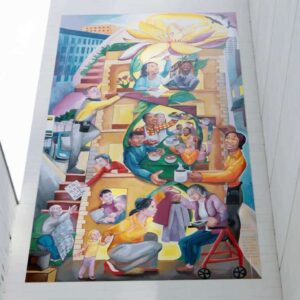 A large mural on a white wall depicts diverse people engaging in community activities, with a giant yellow flower at the top and a cityscape background.