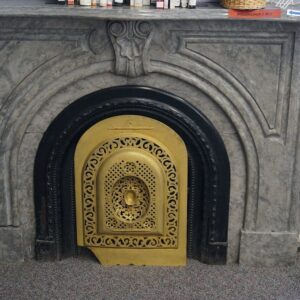Ornate gray marble fireplace with a decorative gold metal insert and carved details, set against a light purple wall with items placed on the mantel.