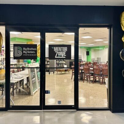 Entrance to a “Mentor Zone” room, decorated with gold number 5 balloons and green and black balloon clusters; Big Brothers Big Sisters signs are visible through glass doors.