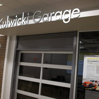 Exterior view of the Kulwicki Garage, featuring a glass garage door and a poster about a NASCAR drawing event on the right side of the entrance.