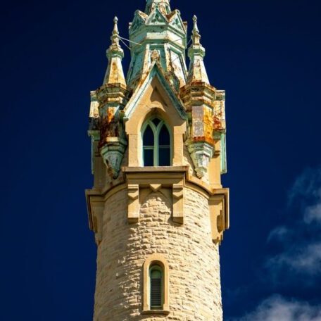 Stone tower with ornate, weathered copper details and arched windows against a deep blue sky.