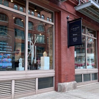 Brick building with large windows displaying art and a sign for an exhibit titled “Forward V: Our Wisconsin & Regional Artists” at the In Art House gallery.