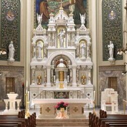 Interior view of a church featuring ornate altars, religious statues, decorative columns, chandeliers, and wooden pews arranged facing the altar.