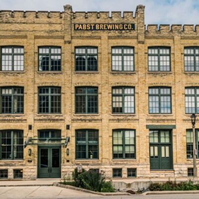 A three-story brick building with many windows and a sign reading “Pabst Brewing Co.” above the entrance.